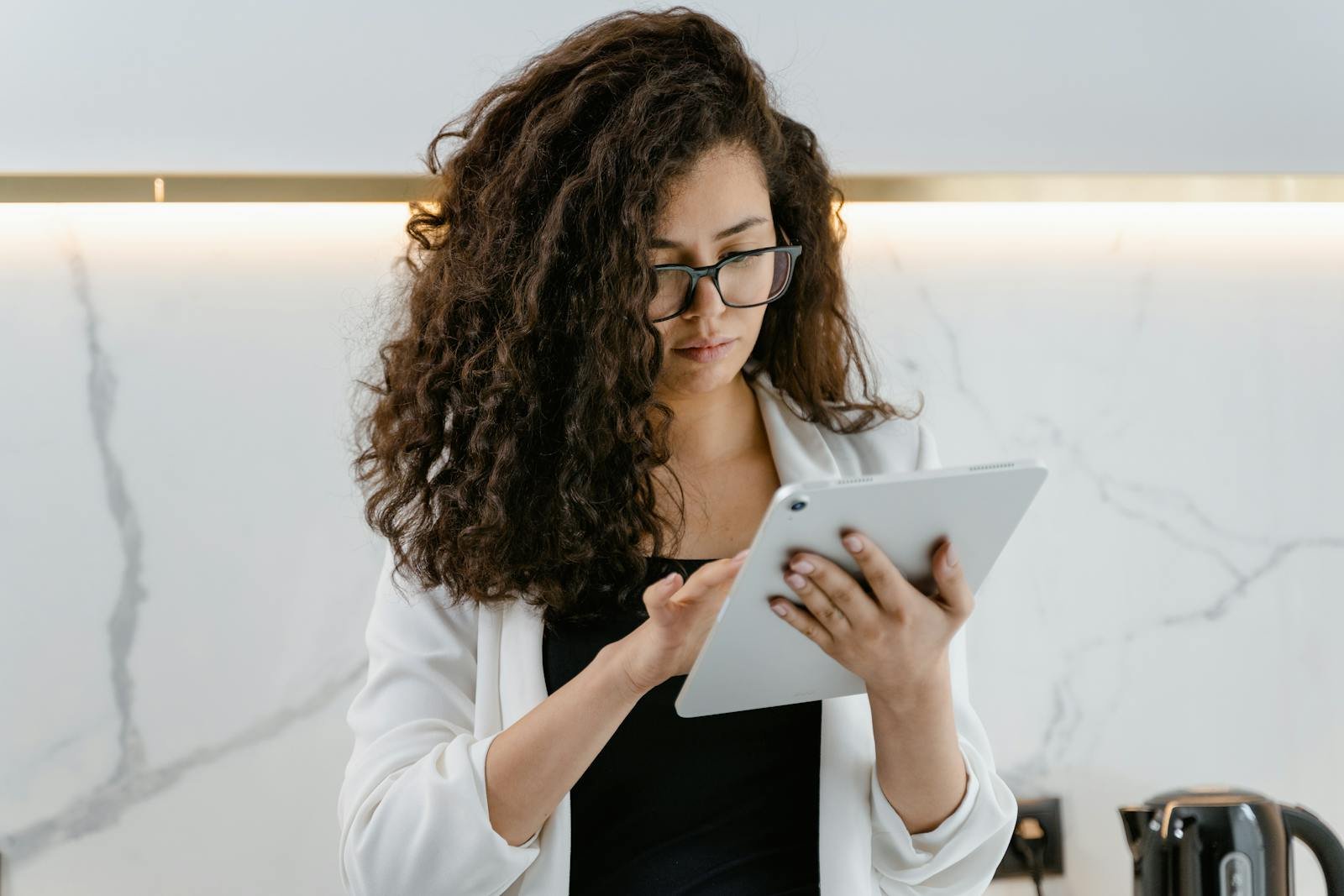 A woman uses a tablet in a modern kitchen, focusing on technology and multitasking.